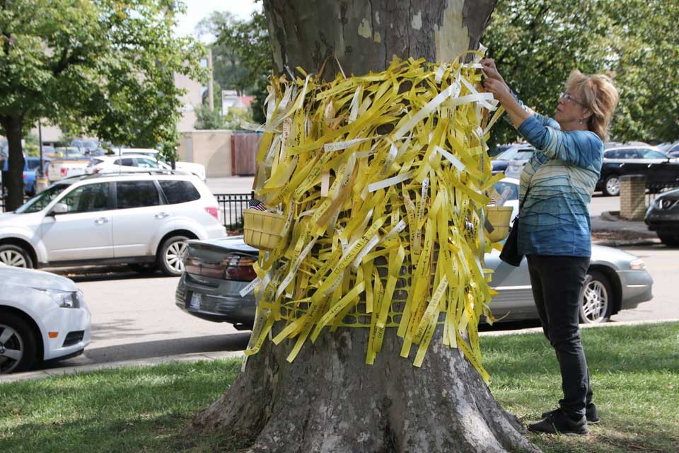 ArtPrize visitor tying a yellow ribbon with message to a tree in Veterans Memorial Park during ArtPrize 2021