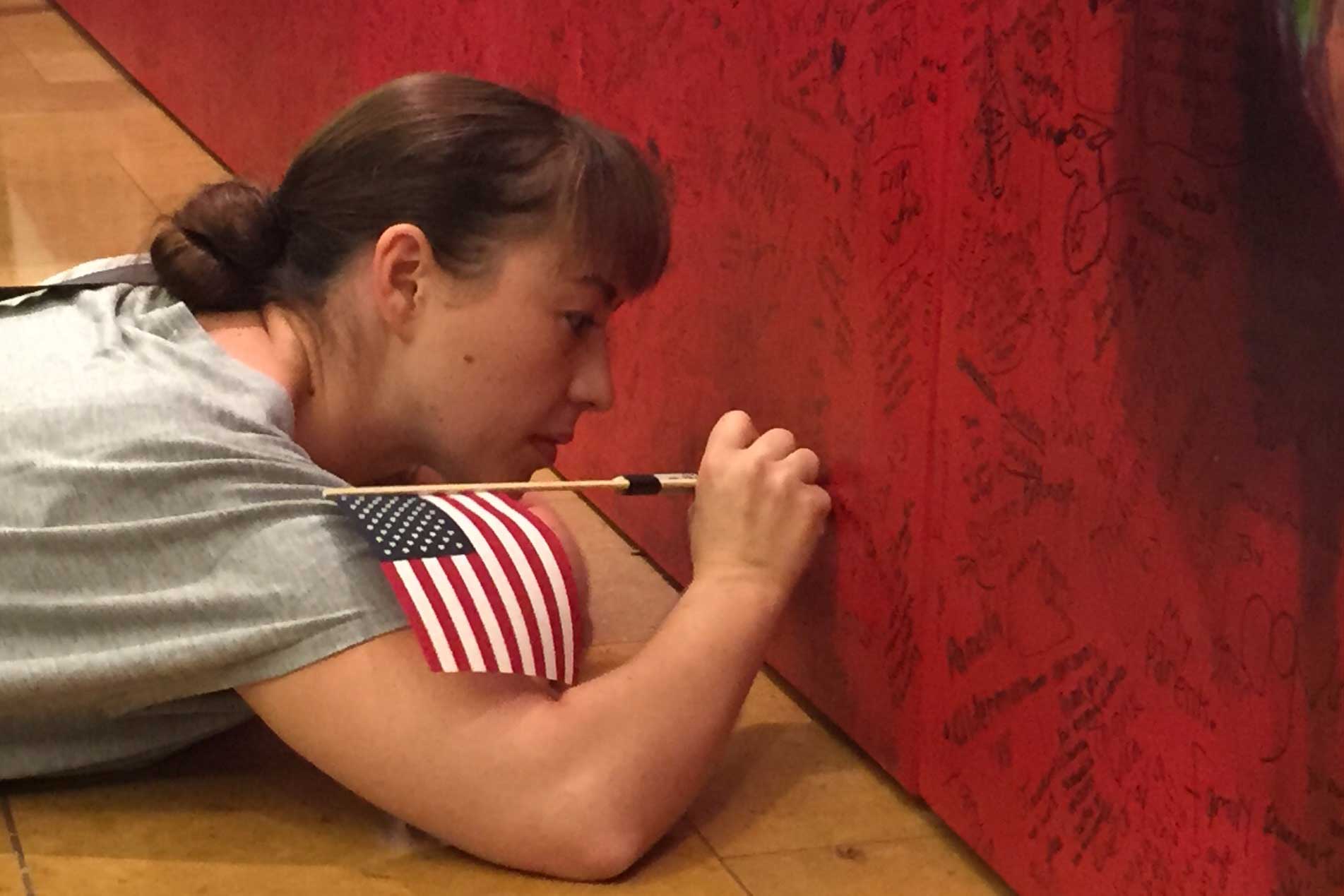 A young woman on floor writing her hero message on Hometown Hero during ArtPrize Seven