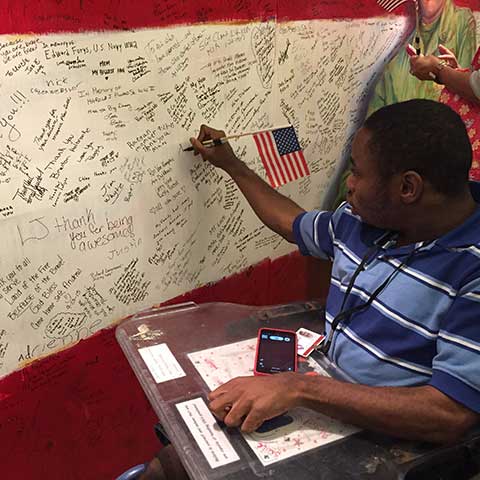 Young man in wheelchair writing hero message on Hometown Hero installation at ArtPrize Ten